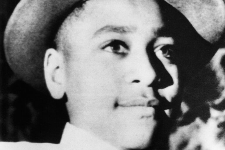 a black and white photo of Emmett Till shows him smiling and wearing a hat