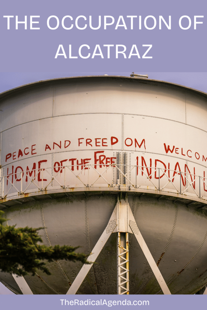 a water tower with red graffiti says "Peace and Freedom Welcome, Home of the Free Indian Land"